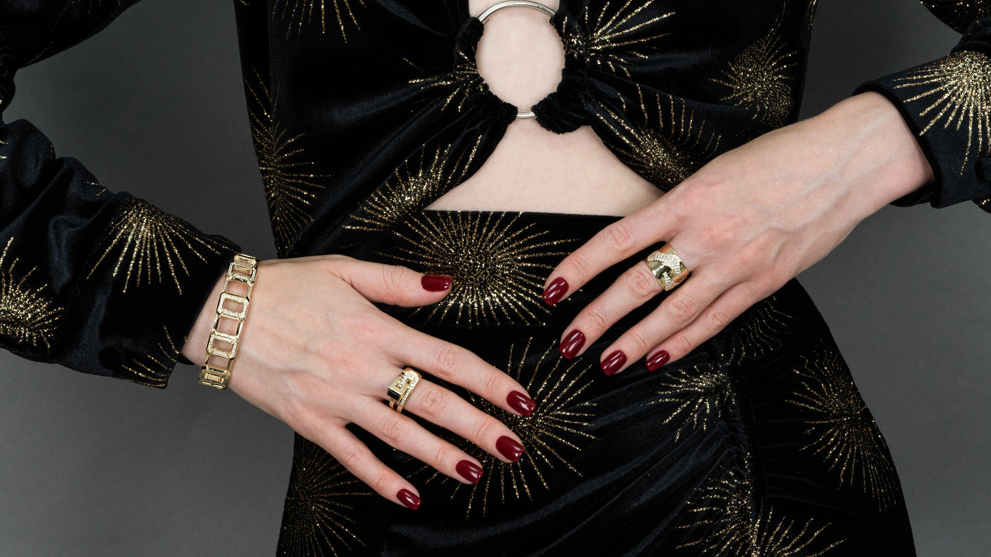 Woman wearing Solidarité bracelet & rings showcasing jewelry against an elegant black and gold dress.
